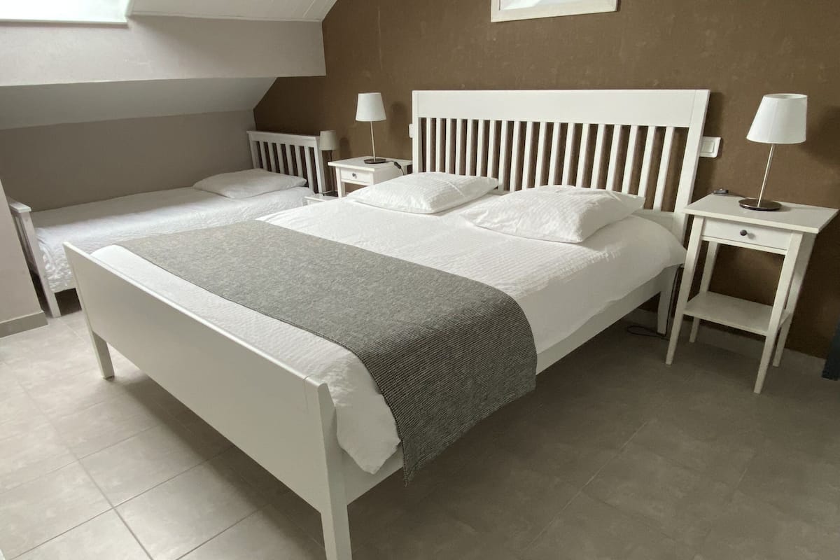 Un lit double avec un couvre-lit gris, une tête de lit blanche et des tables de chevet avec des lampes.
