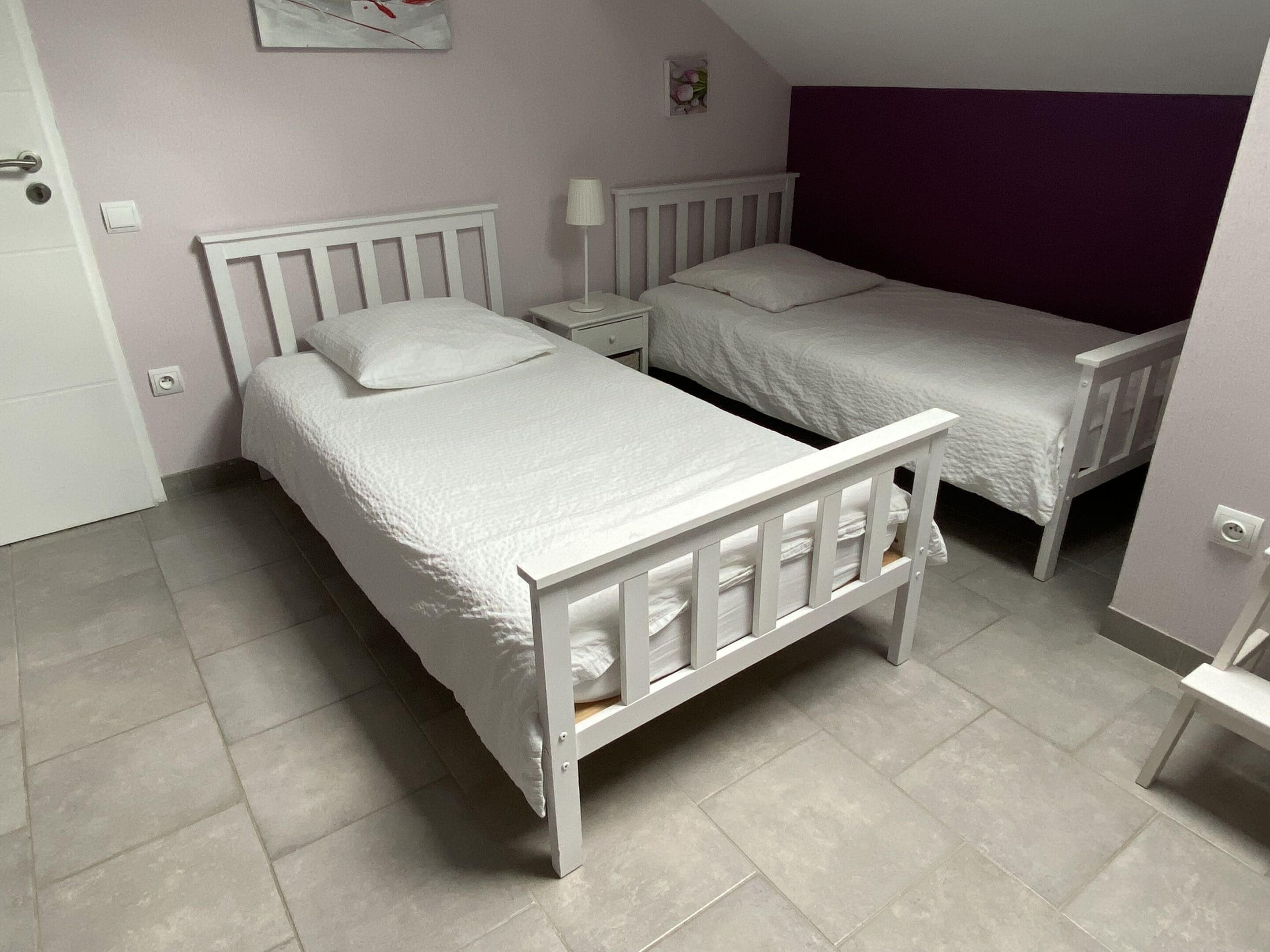 A bedroom with two single beds, a nightstand, a lamp, and a small picture frame on the wall.