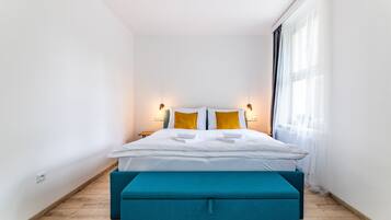 A modern hotel room with a neatly made bed, two bedside tables, and a large window with sheer curtains.