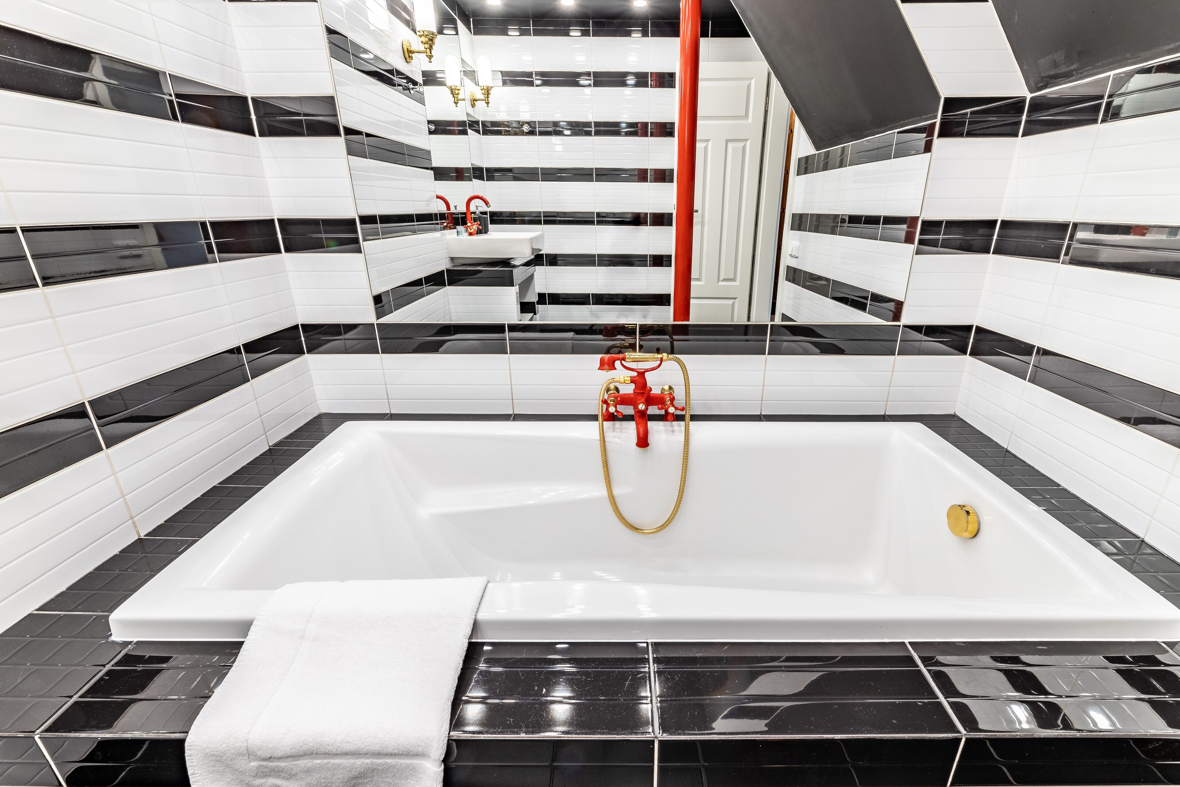 A modern bathroom with a large bathtub, black and white tiled walls, and a red towel.