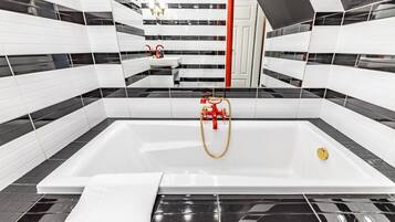 A modern bathroom with a large bathtub, black and white tiled walls, and a red towel.