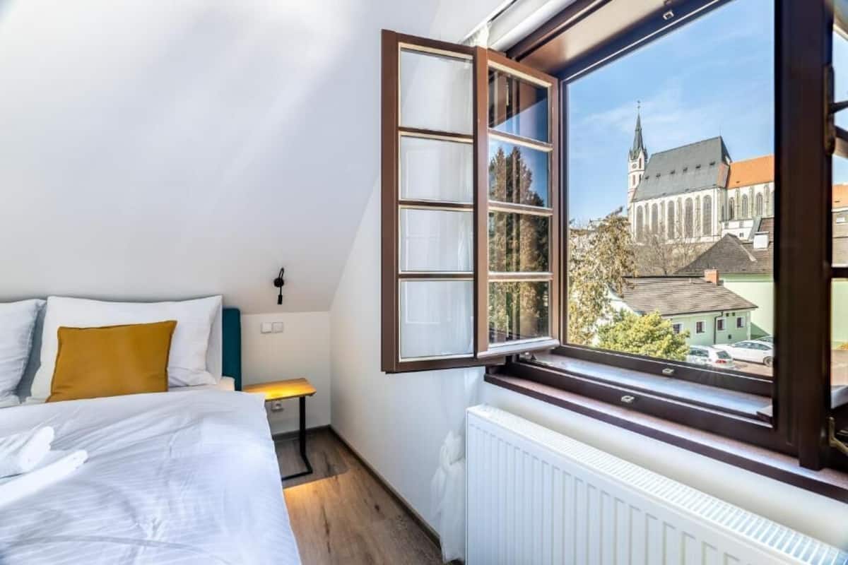 A bedroom with a large window, a bed, a bedside table, and a radiator.