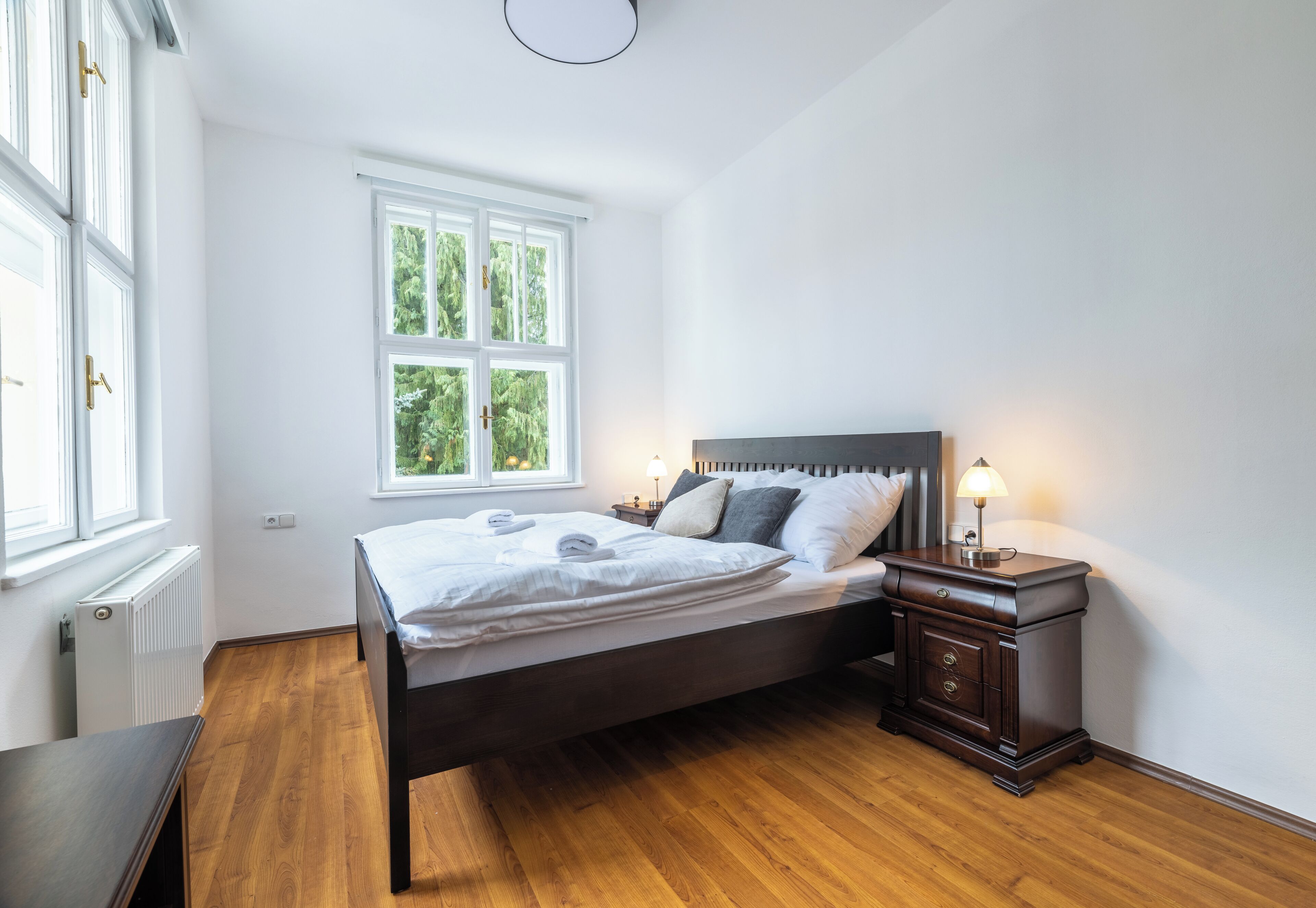 A bedroom with a bed, bedside tables, a window, and a radiator.