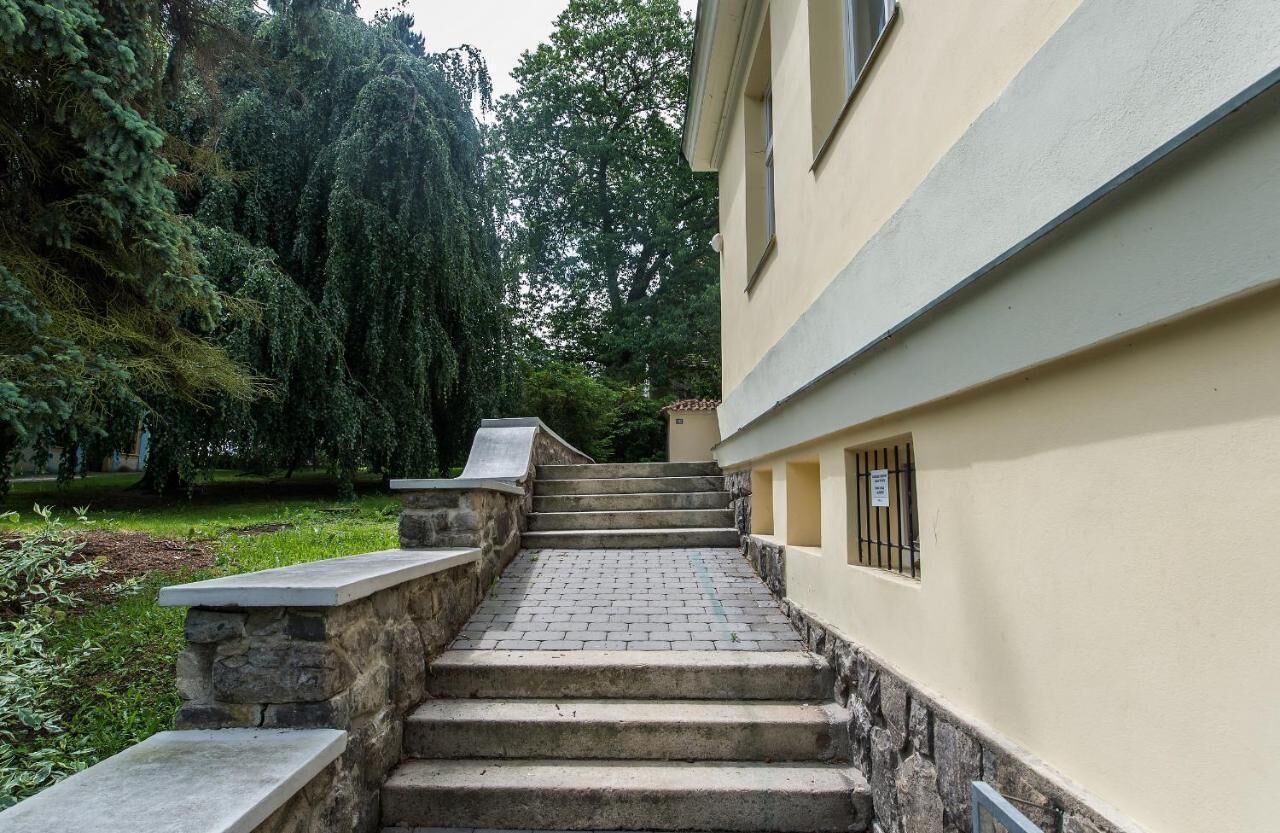 A stone staircase leading to a building with a stone wall on one side and a tree-lined garden on the other.