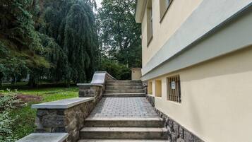 A stone staircase leading to a building with a stone wall on one side and a tree-lined garden on the other.