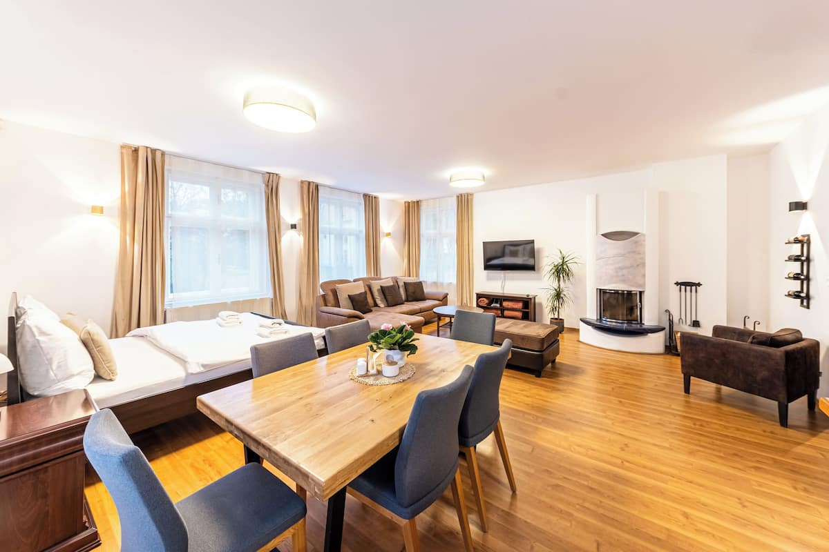 A modern hotel room with a wooden dining table, a sofa, a fireplace, and a TV.