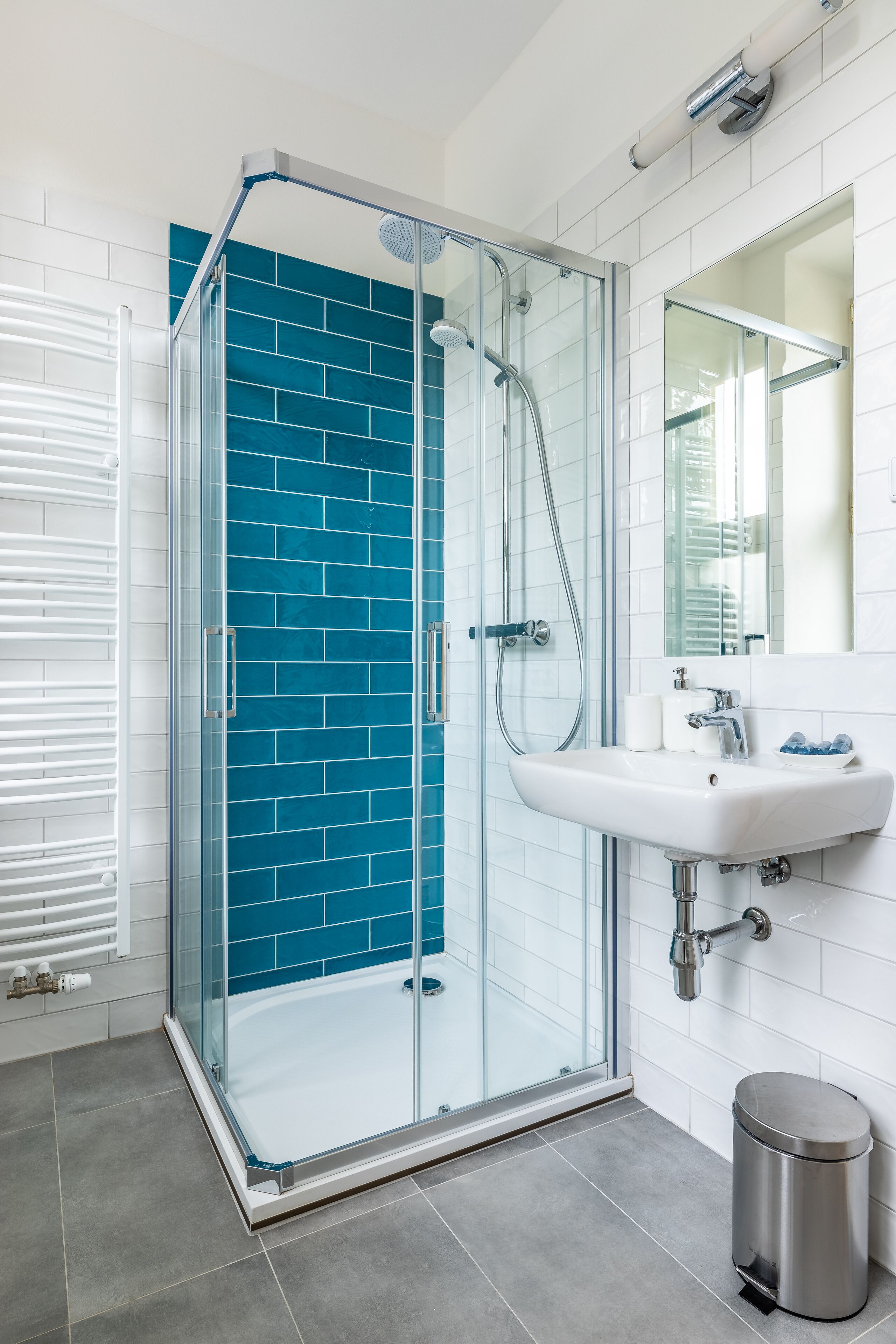 A modern bathroom with a glass-enclosed shower, white tiles, and a sink with a mirror above it.