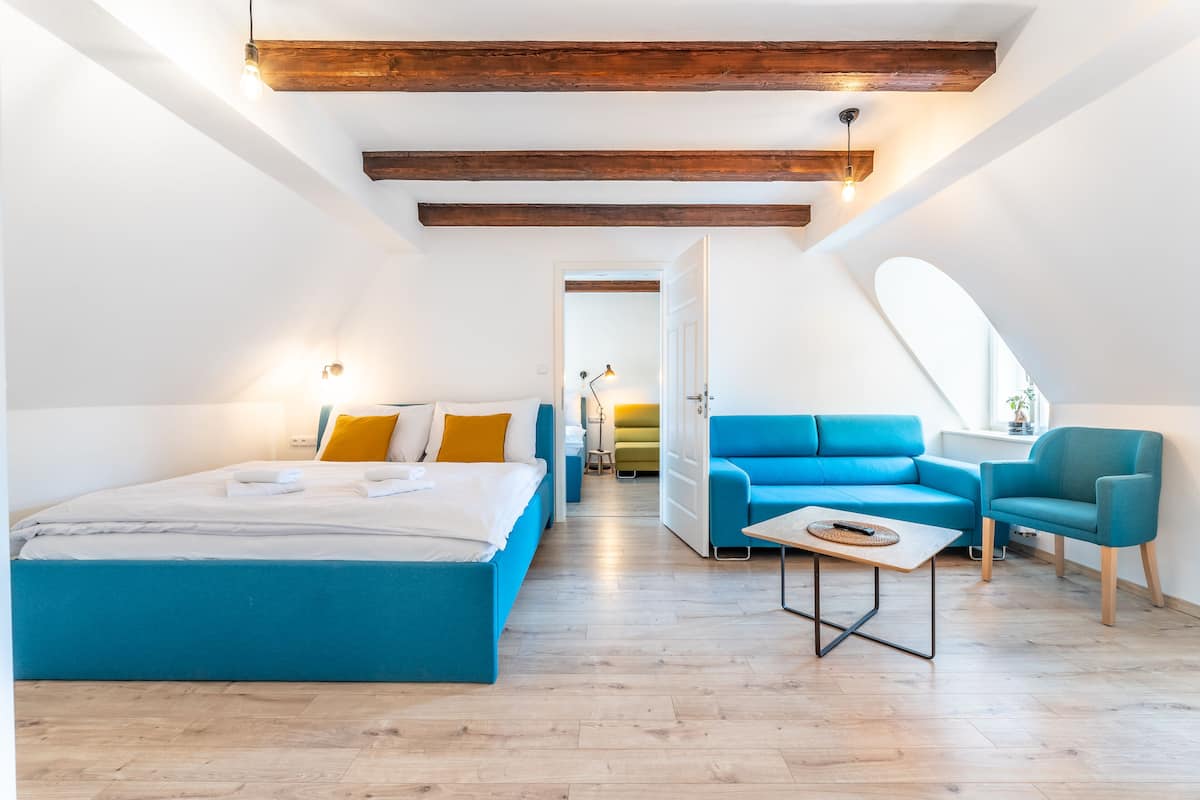 A modern loft bedroom with a large bed, a blue sofa, and a small table.