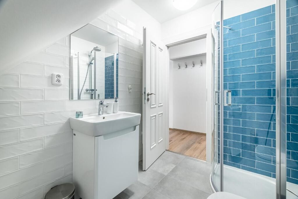 Un baño con lavamanos blanco, espejo y cabina de ducha.