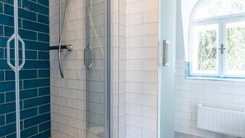 A modern bathroom with a glass-enclosed shower, white tiled walls, and a view of the outdoors through a window.