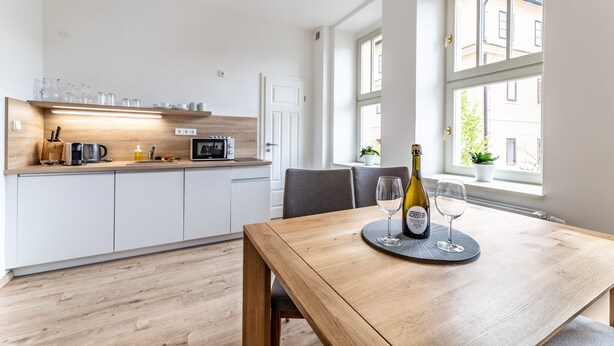 Una cocina moderna con armarios blancos, encimera de madera y comedor con mesa lista para dos comensales.