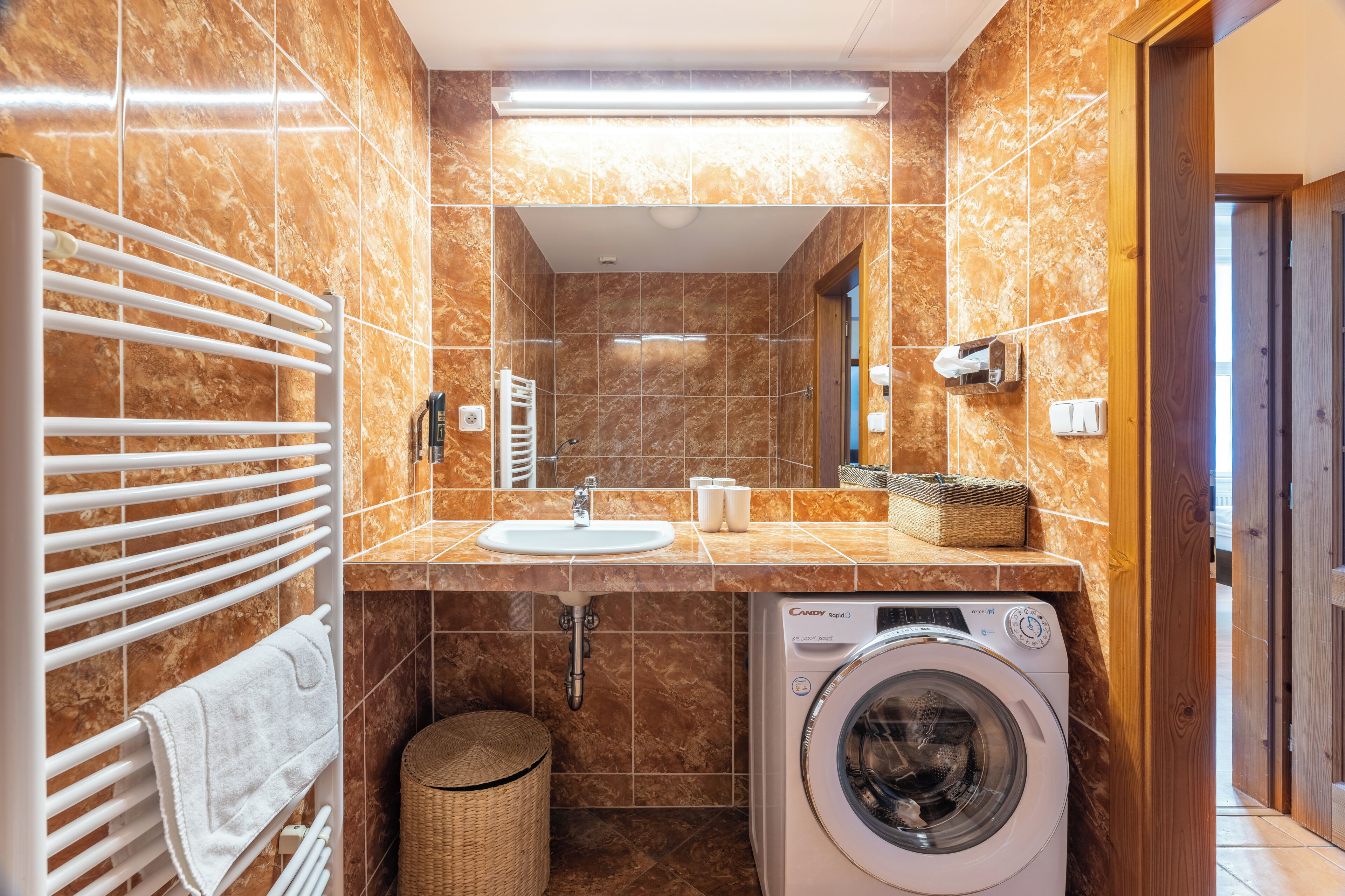 Een badkamer met een wasmachine, een handdoekhouder, een wastafel en een spiegel.