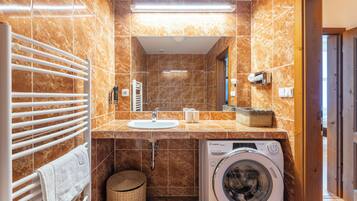 Een badkamer met een wasmachine, een handdoekhouder, een wastafel en een spiegel.