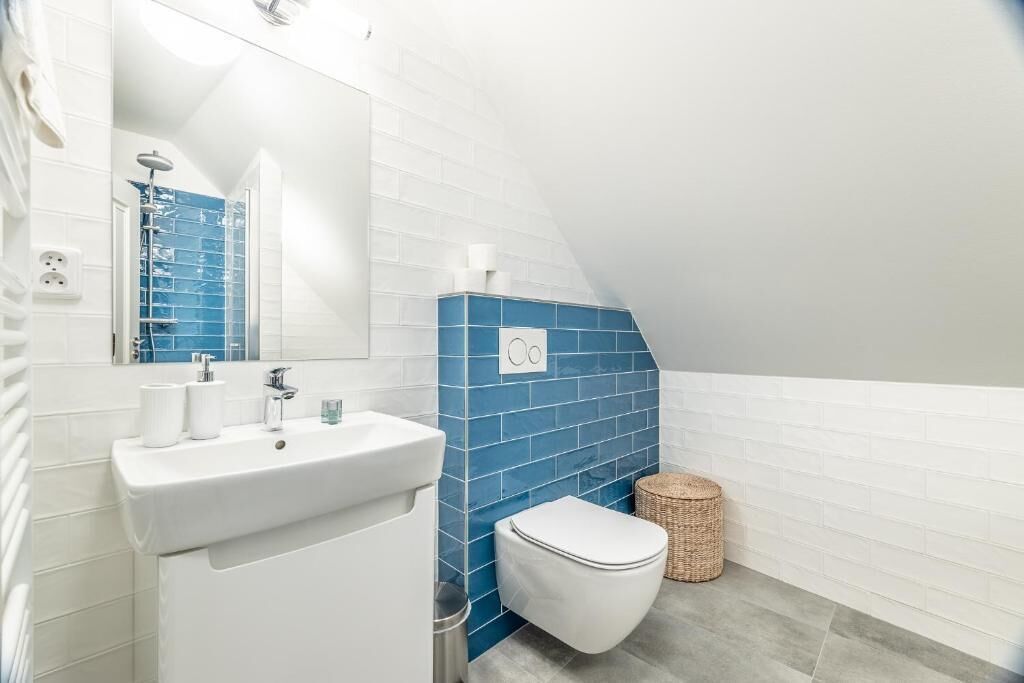 A bathroom with a white sink, a white toilet, a blue-tiled wall, and a mirror.
