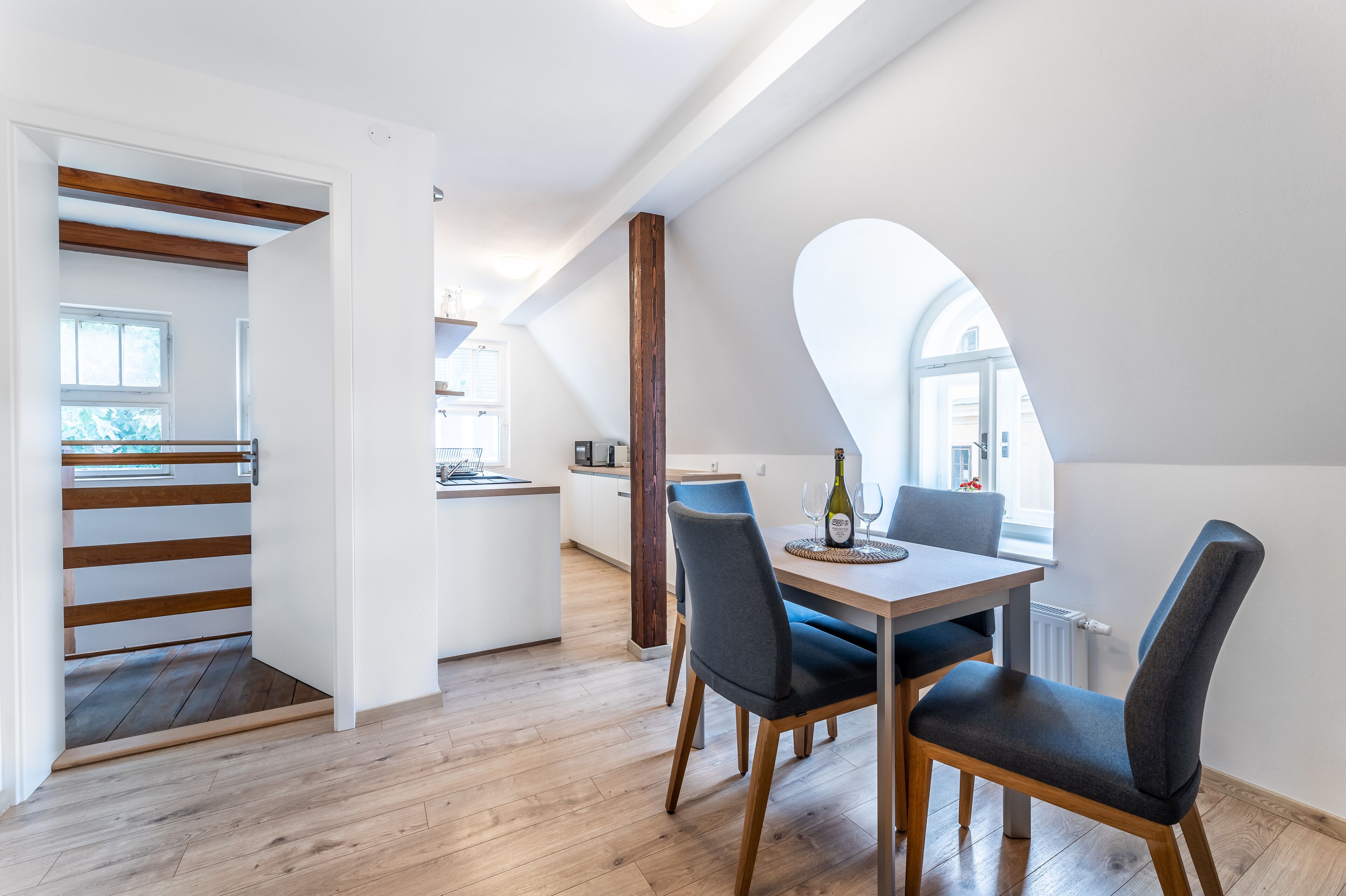 A modern kitchen with wooden flooring, a dining area with a table and chairs, and a staircase leading to an upper level.