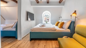 Un dormitorio con cama, televisión, ventana y lámpara.