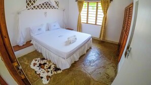 A bedroom with a bed, a window with curtains, an air conditioning unit, and a ceiling fan. - Doric Cottages Diani (Diani Beach)