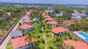 Un resort con varias edificaciones tipo cabaña, una piscina y abundante follaje.