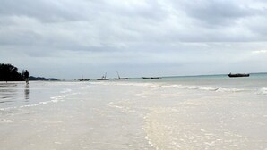 A beach with calm waters and boats in the distance. - Doric Cottages Diani (Diani Beach)