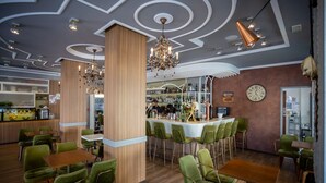 Un restaurant doté d’un bar, de chaises recouvertes d’un tissu vert et d’une colonne en bois.