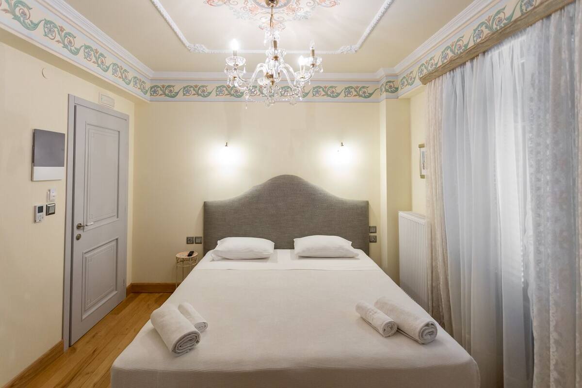 A hotel room with a large bed, a chandelier, a door, and a window with curtains.