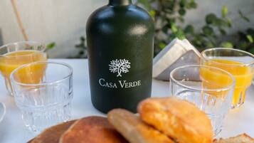 Una botella con la etiqueta "Casa Verde", vasos de jugo de naranja y pan sobre una mesa.