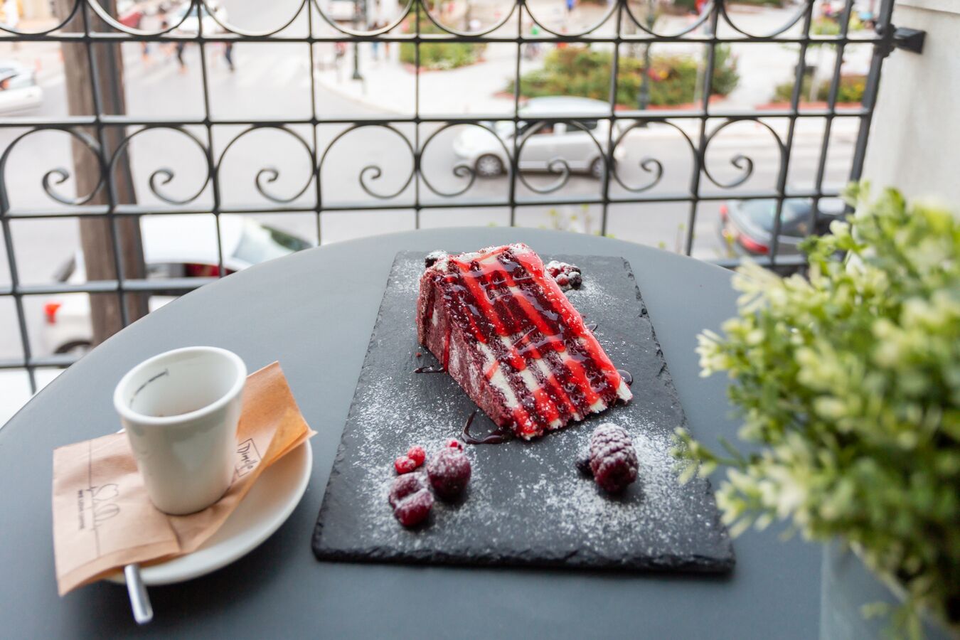 A dessert on a slate plate with a cup and napkin on a table, viewed from a balcony with a metal railing.
