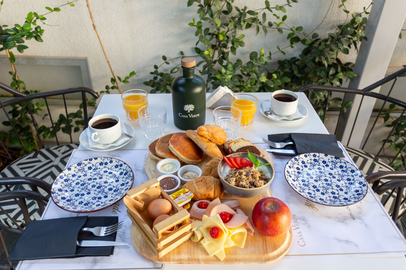 A breakfast table set outdoors with a variety of foods, drinks, and a bottle of Casa Verde olive oil.