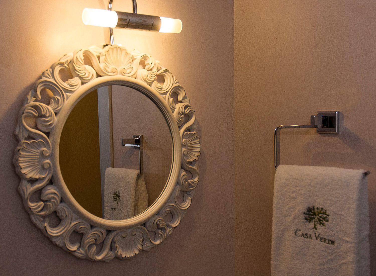 A bathroom with a round mirror, a towel rack, and a wall-mounted light fixture.