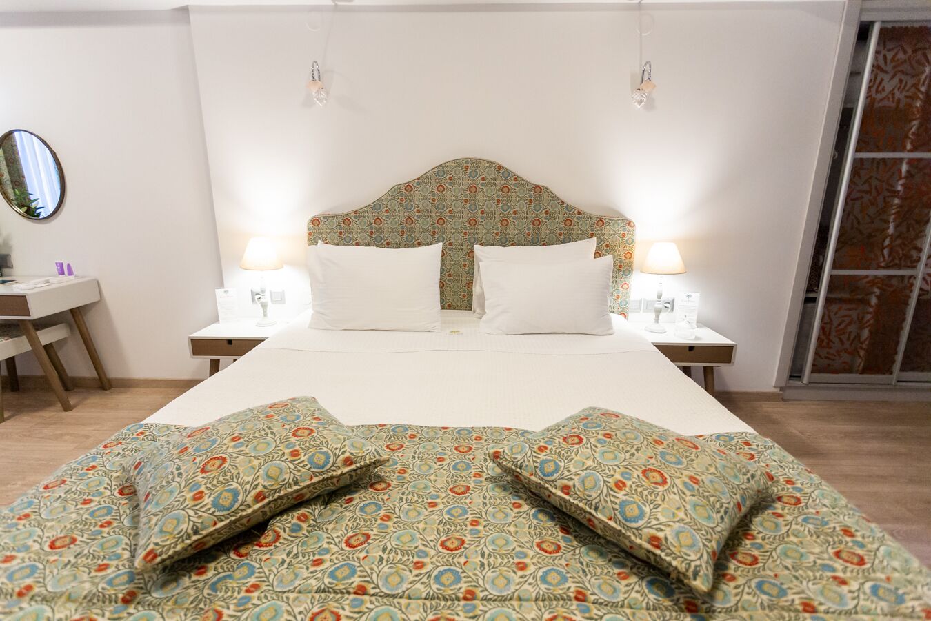 Un lit bien fait, avec une literie à motifs, deux tables de chevet avec des lampes et un miroir au mur.