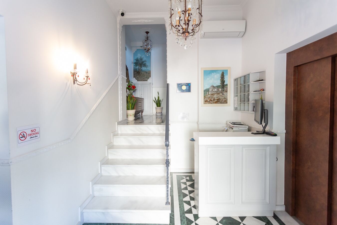 A staircase with white steps leading to a landing, a chandelier, a painting, and a 'No Smoking' sign.
