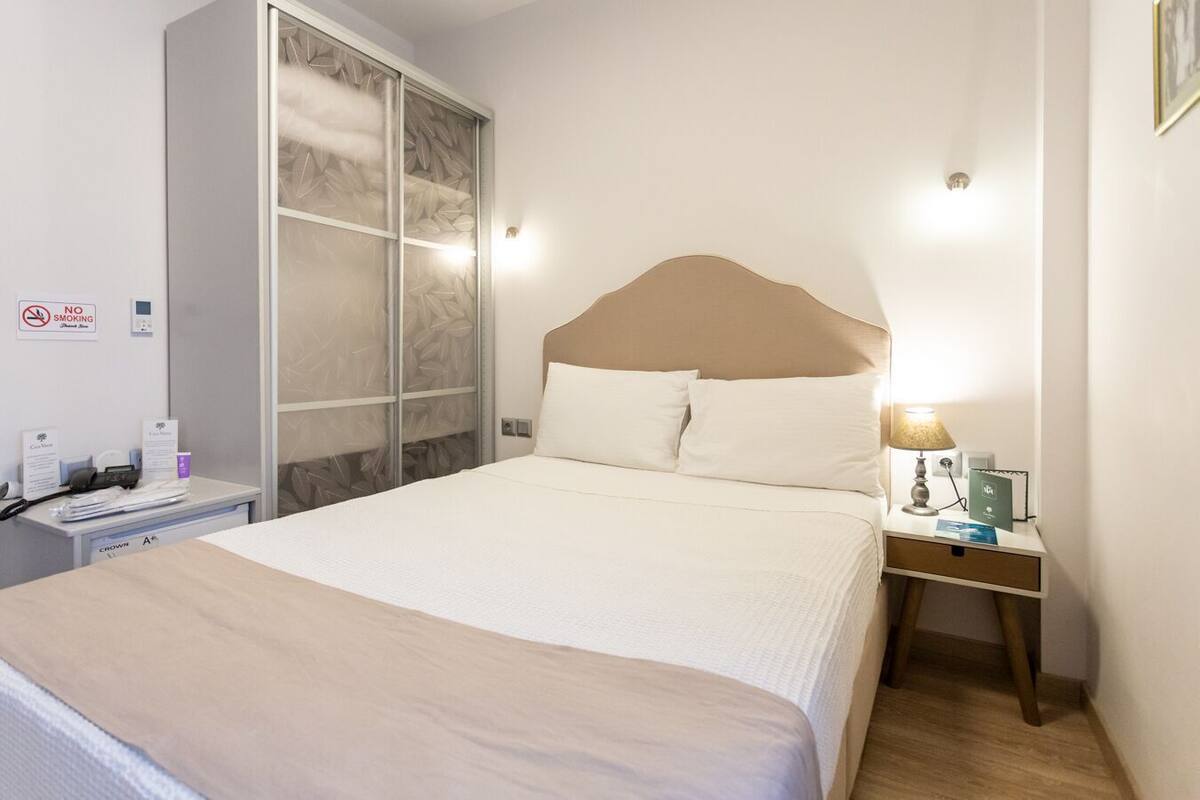A hotel room with a bed, a nightstand, a lamp, a wardrobe, and a 'No Smoking' sign.
