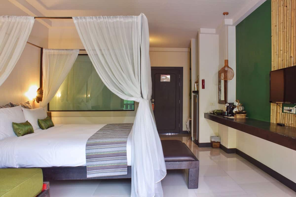 A hotel room with a bed, a bench, a TV, and a green wall.