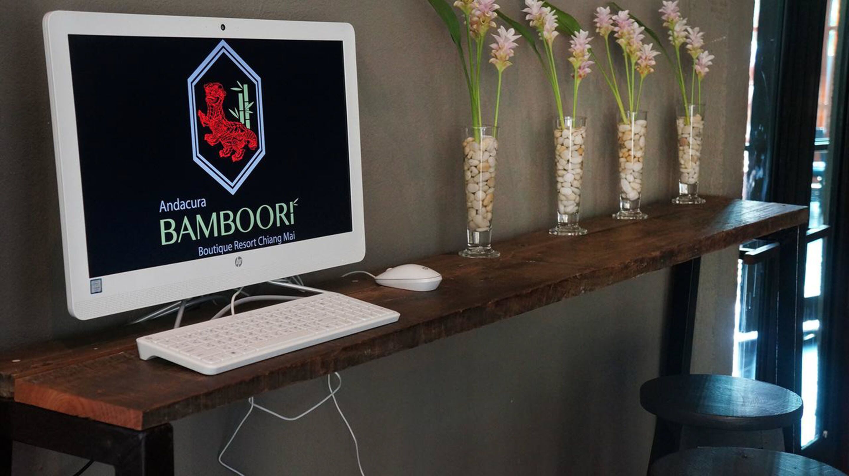 En stationär dator med en bildskärm som visar en logotyp, ett tangentbord, en mus och en trähylla med vaser fulla av blommor.