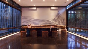 Uma área de bar moderna com um balcão comprido, banquetas de madeira e um grande mural abstrato na parede.
