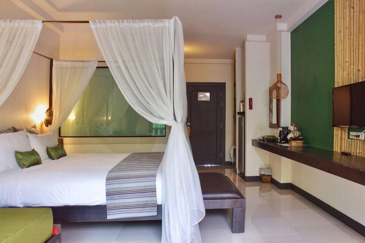 A hotel room with a bed, a bench, a desk, and a television.