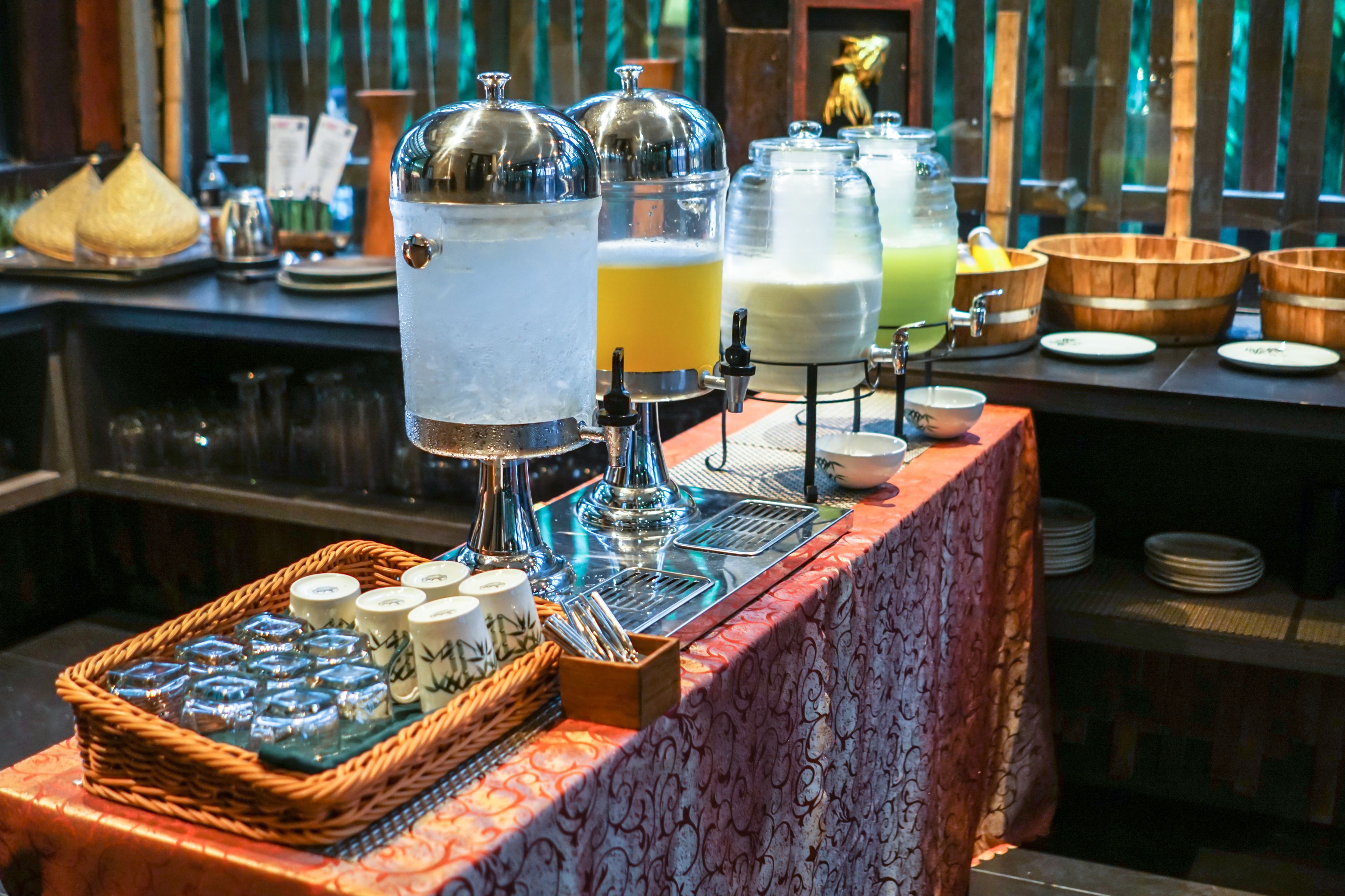 Uma área de bar com um dosador de bebidas, um cesto de canecas e uma mesa de madeira.