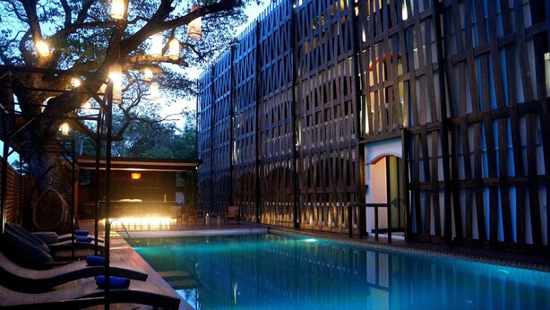 Um hotel moderno com área de piscina, apresentando uma grande piscina ao ar livre, espreguiçadeiras e um edifício com fachada de madeira única.