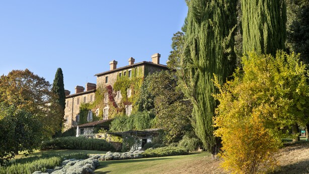 A large, historic building with a garden in front, featuring a pond, neatly trimmed hedges, and tall trees. - Azienda Agricola Chiarentana (Chianciano Terme)