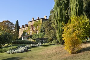 A large, historic building with a garden in front, featuring a pond, neatly trimmed hedges, and tall trees. - Azienda Agricola Chiarentana (Chianciano Terme)