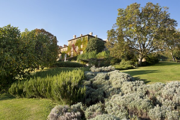 A large, historic building with a well-maintained garden featuring various shrubs and trees. - Azienda Agricola Chiarentana (Chianciano Terme)