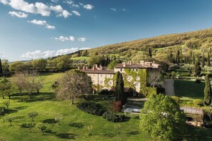 A stone building with a tiled roof, surrounded by a well-maintained garden and a hilly landscape.