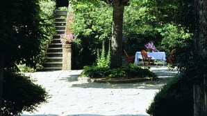 A stone staircase leading up to a brick archway, surrounded by lush greenery and a table with chairs set under a tree. - Azienda Agricola Chiarentana (Chianciano Terme)
