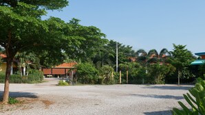 A gravel parking area with a building in the background, surrounded by trees and greenery. - Kwanjai Resort (Tha Mai)