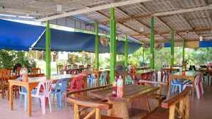 An outdoor restaurant with wooden tables and colorful plastic chairs, covered by a blue canopy. - Kwanjai Resort (Tha Mai)