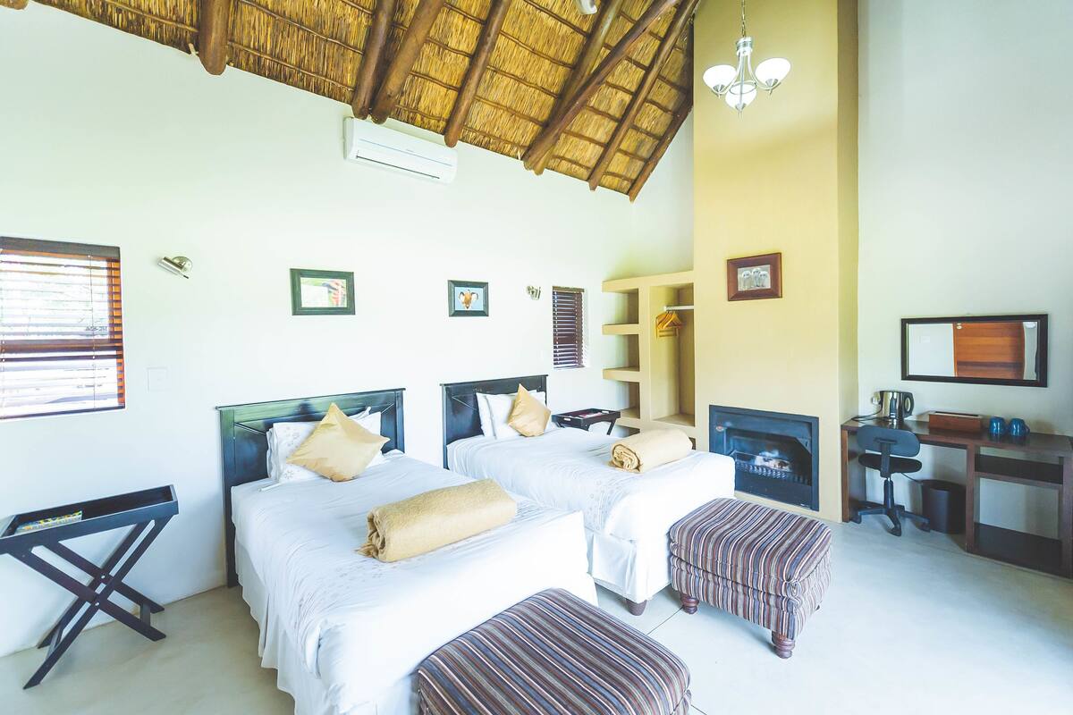 A hotel room with two beds, a desk, a chair, a television, and a fireplace.