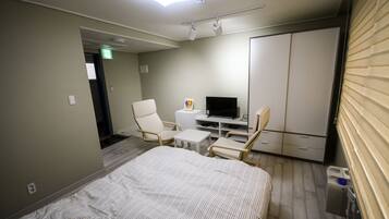 A hotel room with a bed, two chairs, a small table, a TV, and a wardrobe.