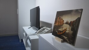 A room with a desk featuring a telephone, a flat-screen TV, and a framed painting of a canal scene. - BLUEHUM Guesthouse - Hostel (Incheon)