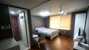 A compact bedroom with a bed, a desk with a computer, a chair, a small table, and a window with blinds. - BLUEHUM Guesthouse - Hostel (Incheon)