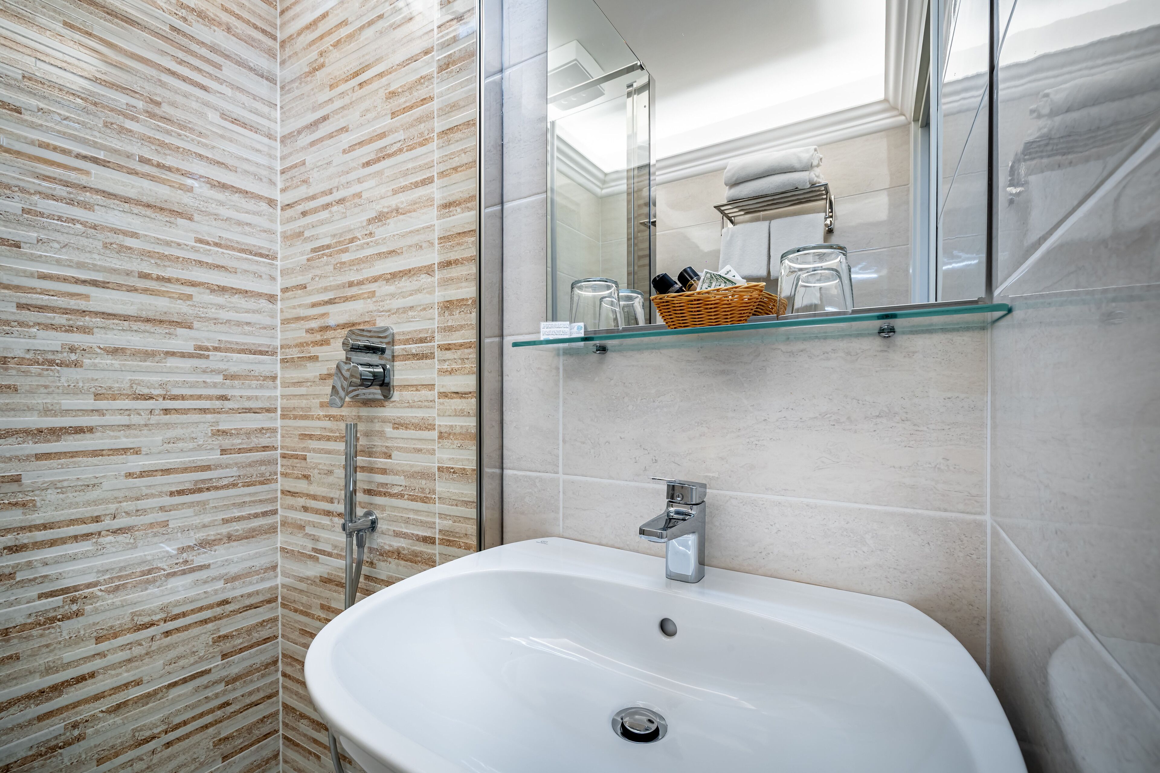 A bathroom with a glass shelf holding toiletries, a white sink, and a shower area with a glass door.